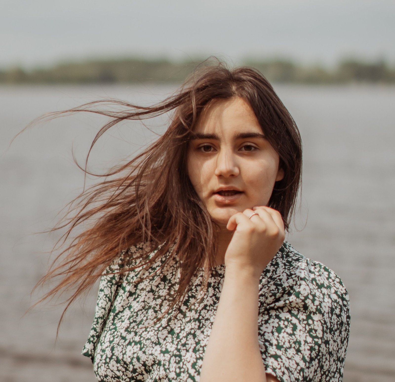 Portrait of a young woman with windblown hair at a lakeside, capturing a serene and natural moment.
